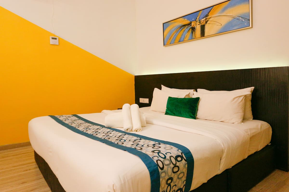 A hotel room with a bed, a painting on the wall, and a bedside table.