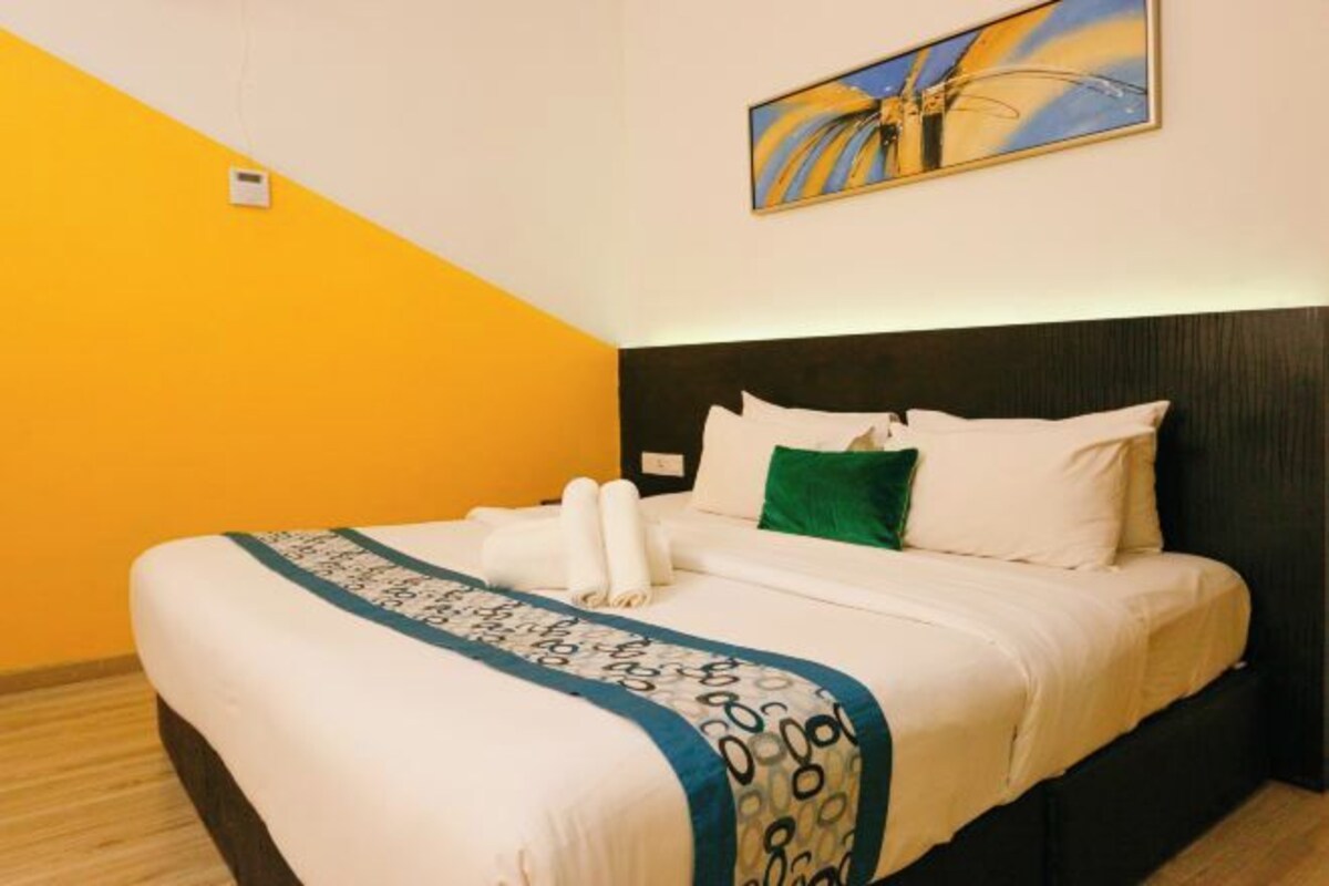 A hotel room with a bed, a painting on the wall, and a yellow accent wall.