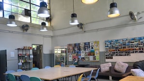 Um quarto espaçoso com uma mesa comprida e cadeiras, uma geladeira, uma estante de livros e um painel decorado com fotos.