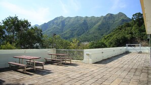 Terraço no telhado com mesas de piquenique e vista para montanhas verdes.