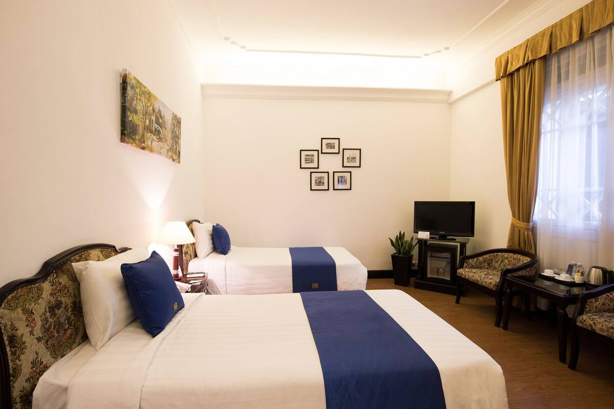 A hotel room with two beds, a TV, a small table with a plant, and a chair.