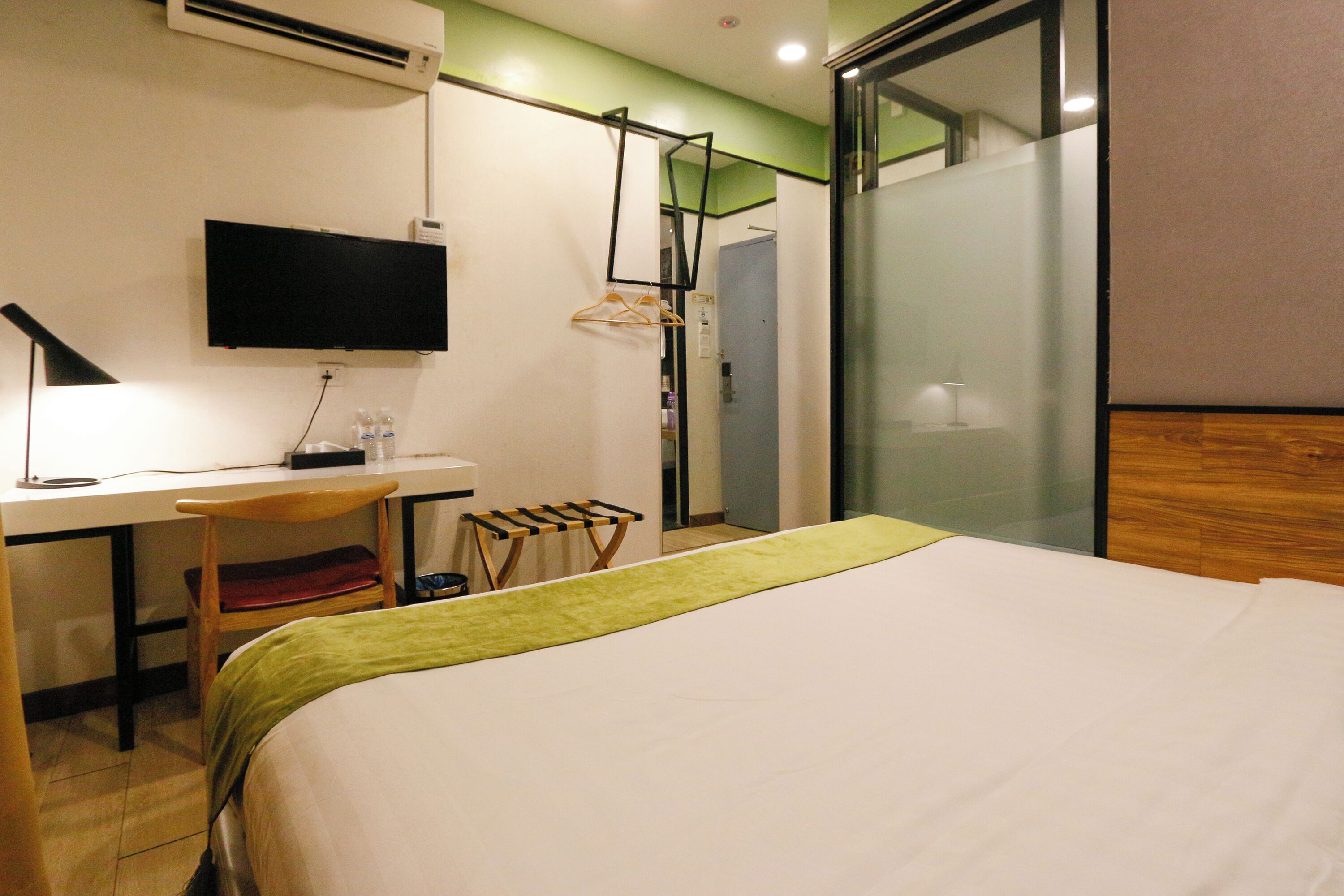 A hotel room with a bed, a desk with a computer, a TV, and a shower area.