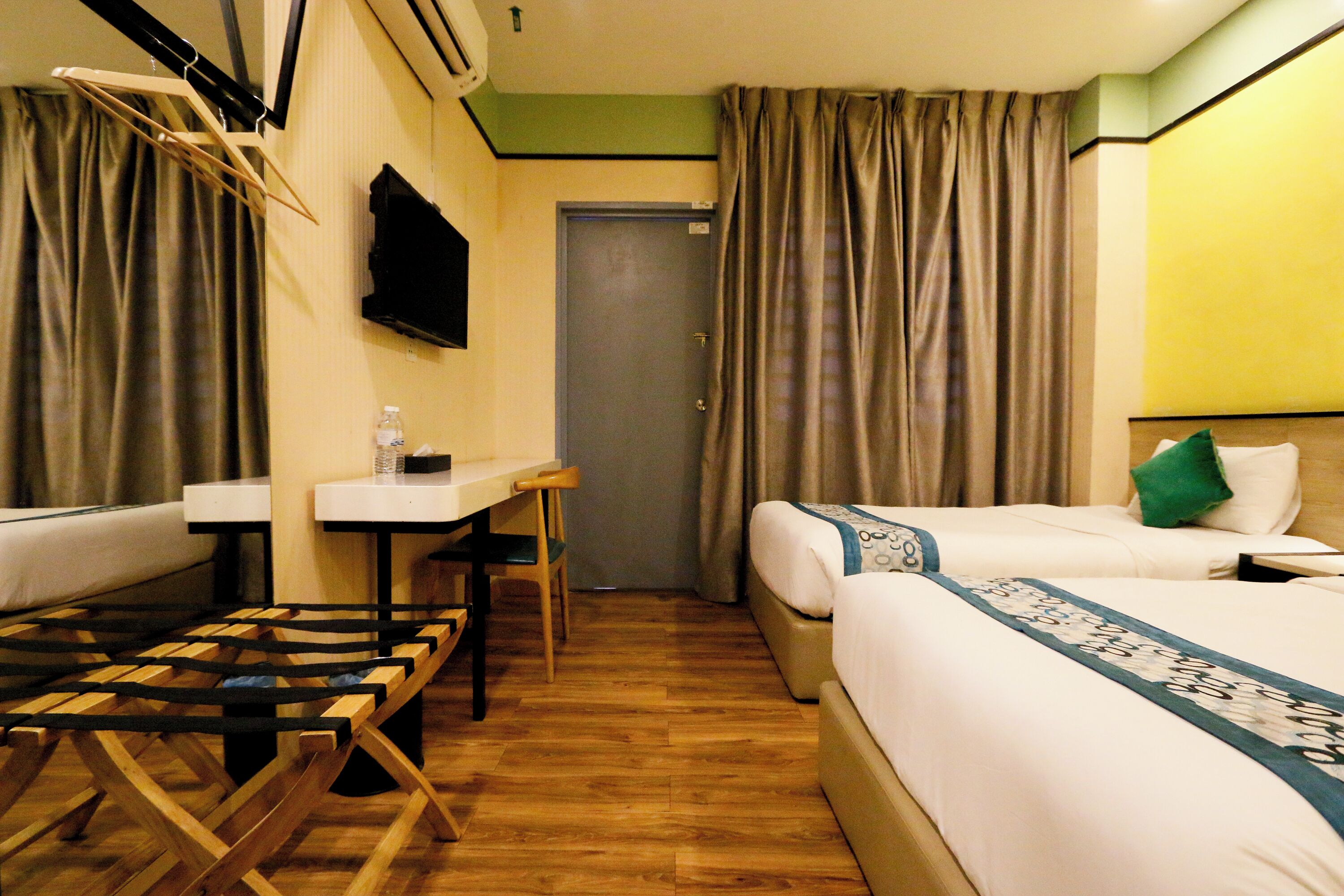A hotel room with two beds, a desk, a chair, and a TV mounted on the wall.