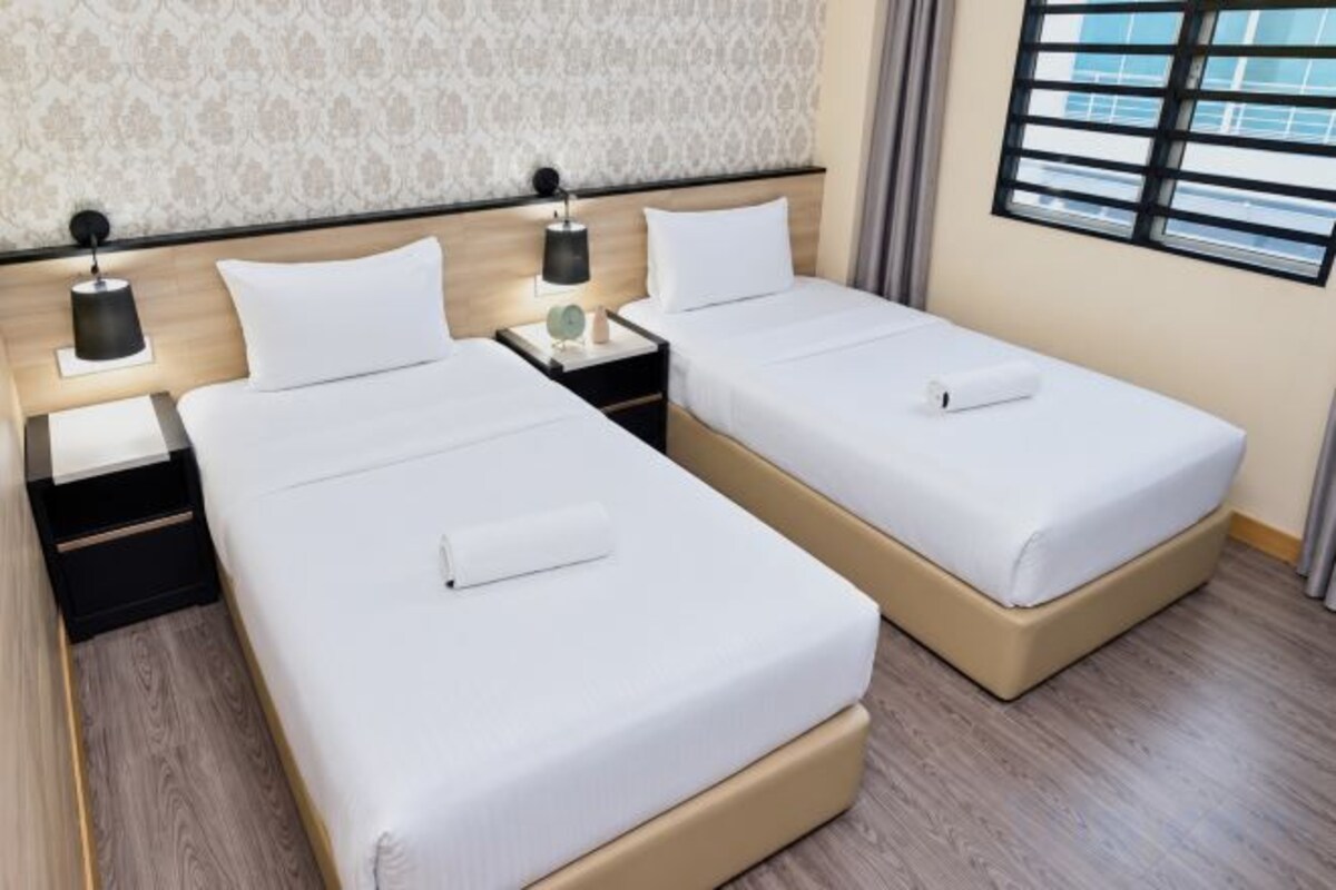 A hotel room with two beds, each with a pillow and a small bedside table with a lamp.