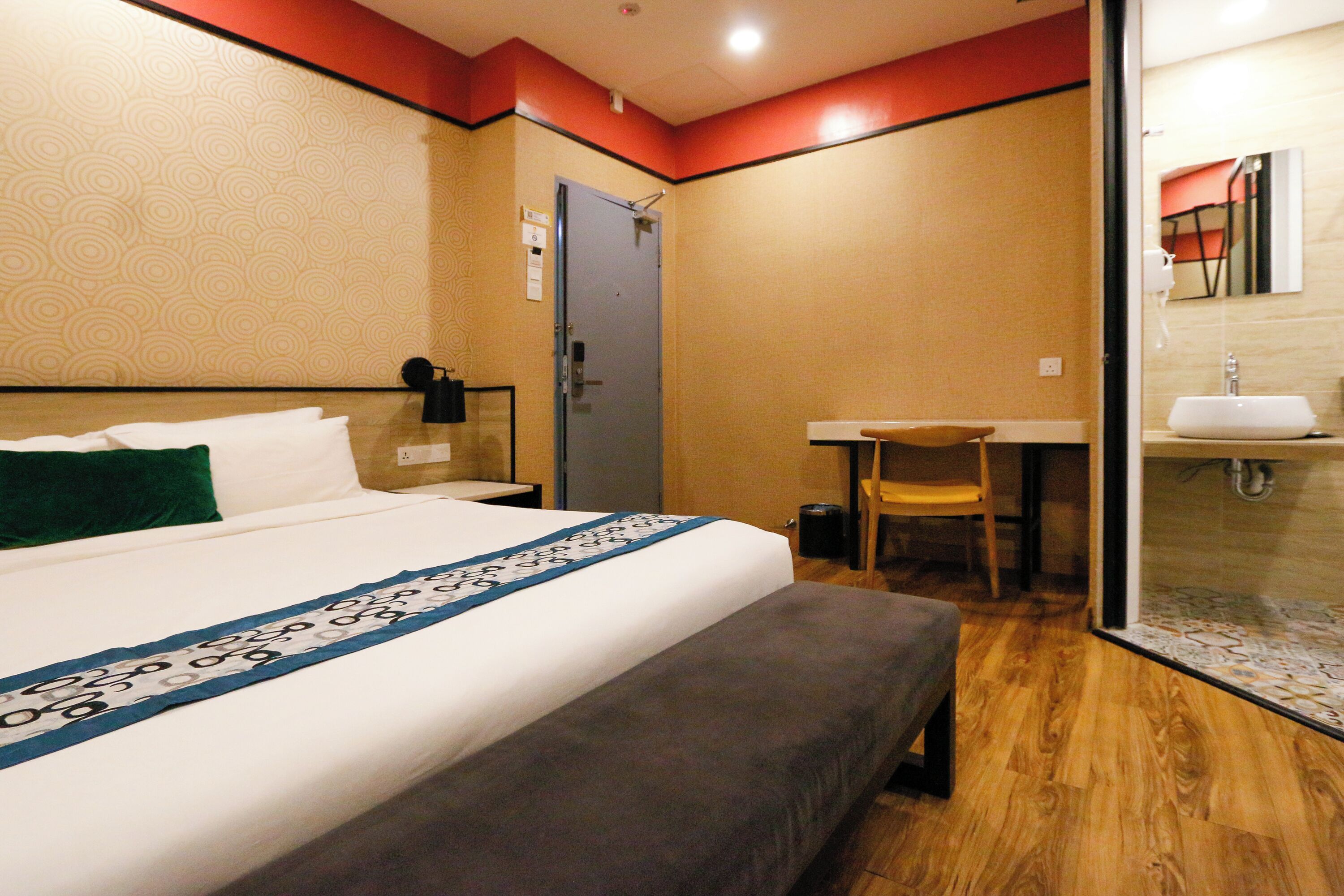 A hotel room with a bed, a desk, a chair, and a bathroom with a sink.