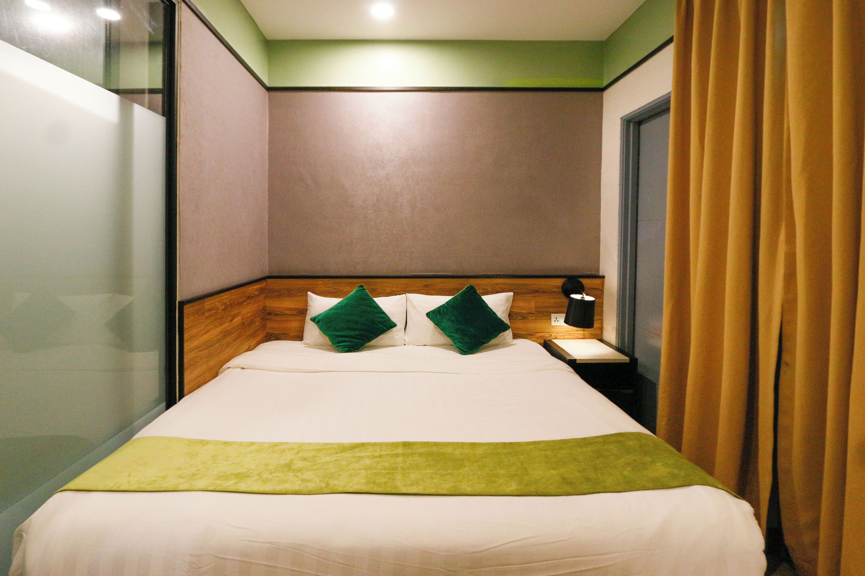 A hotel room with a bed, a nightstand, a lamp, and a window with curtains.