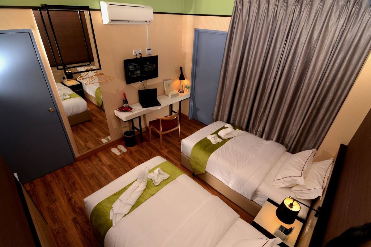A hotel room with two beds, a desk with a computer, a TV, and a mirror.