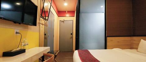 A hotel room with a bed, a desk with a chair, a television, and a door.