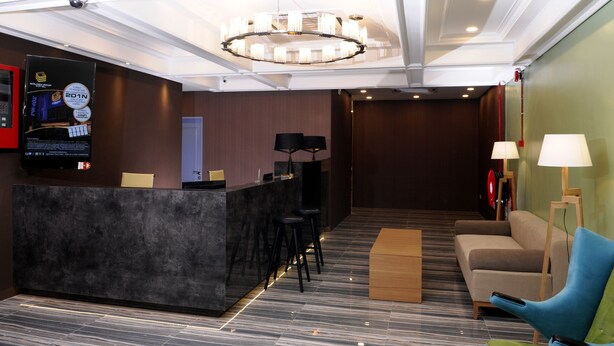 Eine Hotelhalle mit Empfangsschalter, Barhocker, einer Couch und einem Chandelier.