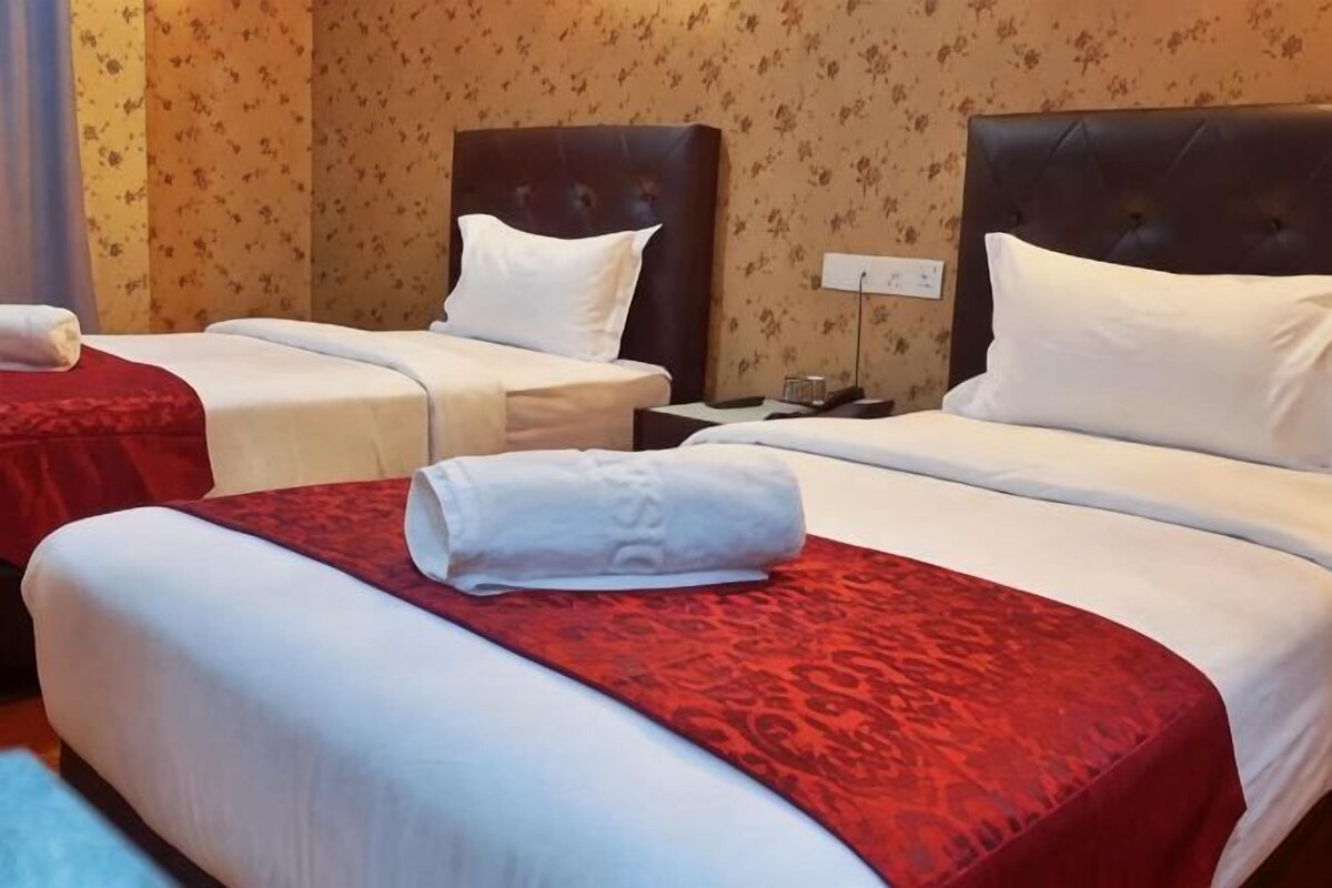 A hotel room with two beds, a nightstand, and a wall outlet.