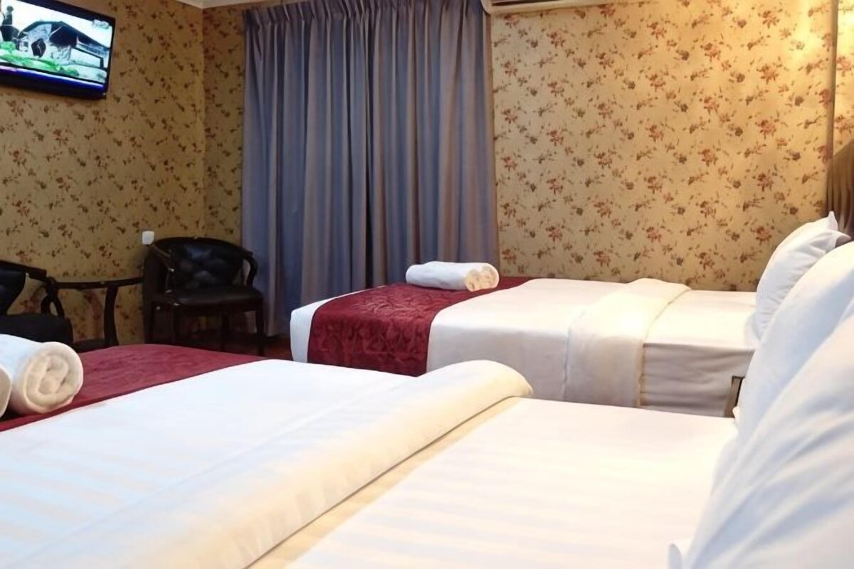 A hotel room with two beds, a television on the wall, and a chair.
