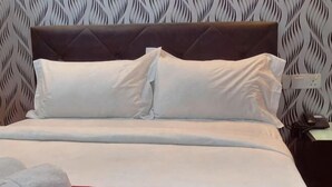 A bed with white bedding, a red accent, and a patterned wall behind it.