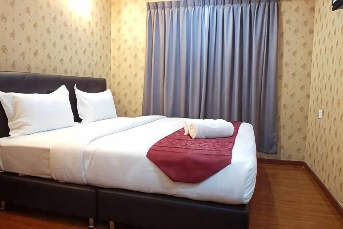 A neatly made bed with white linens and a red throw, a dark headboard, and a window with curtains.