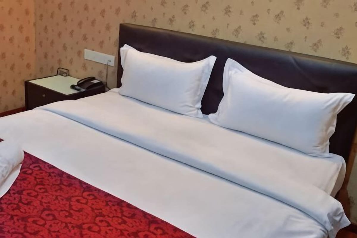 A bed with white linens, a red patterned bedspread, and a dark headboard.
