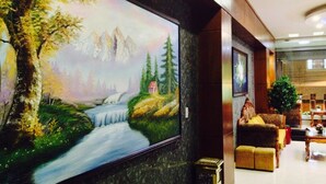 Een lobby met een groot schilderij van een landschap, een receptiebalie en een zithoek met een plant.