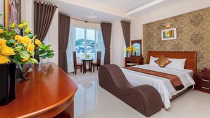Een hotelkamer met een groot bed, een bureau met stoel, een bijzettafeltje met stoelen, en uitzicht op het exterieur.