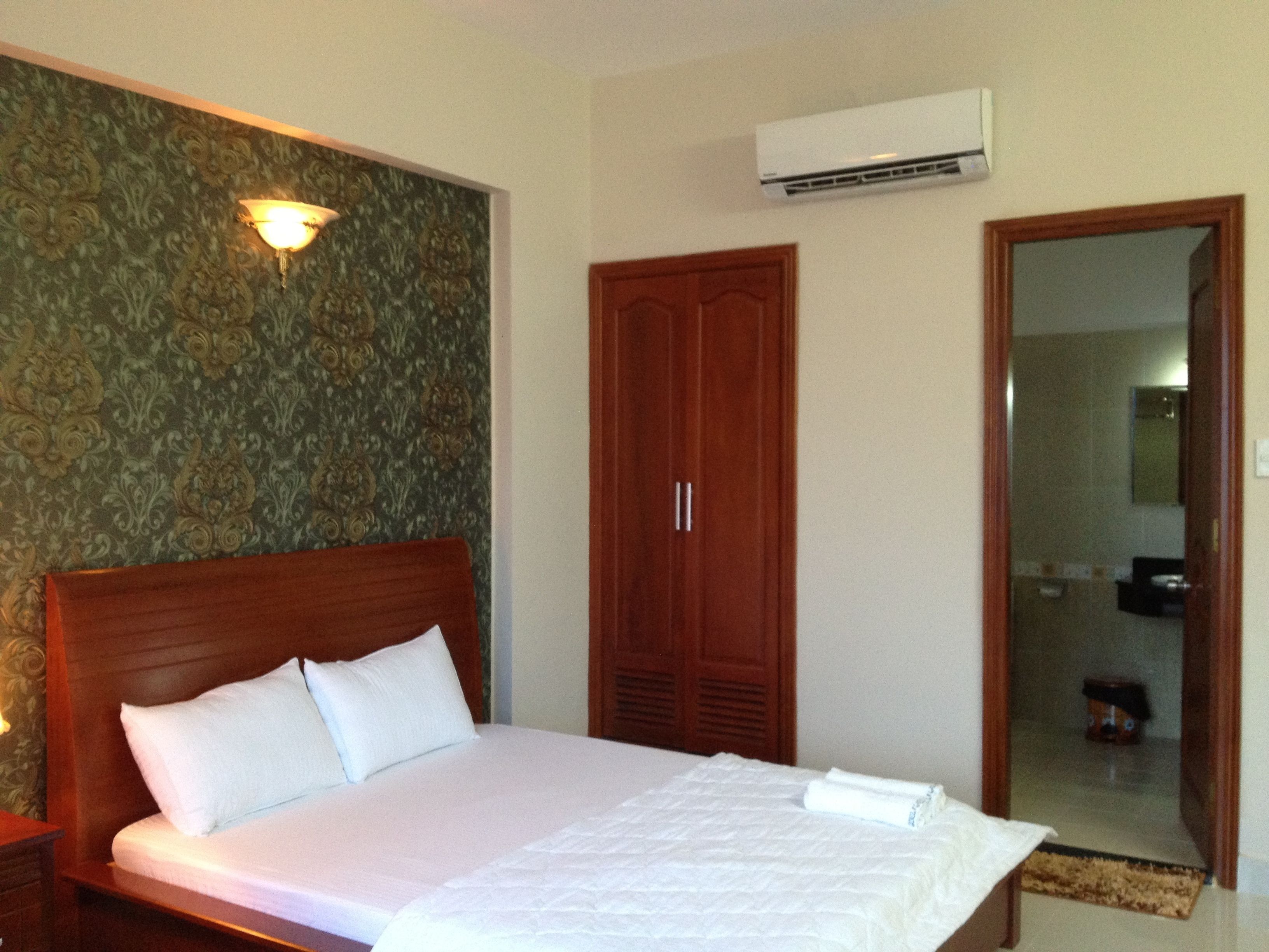 A hotel room with a large bed, a wardrobe, an air conditioning unit, and a mirror.