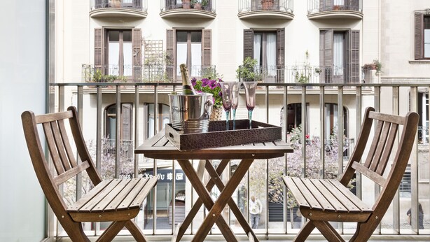 A balcony with two wooden chairs, a small table, and a bottle of champagne.