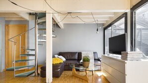 A modern living room with a glass coffee table, a sofa, a TV, and a staircase.