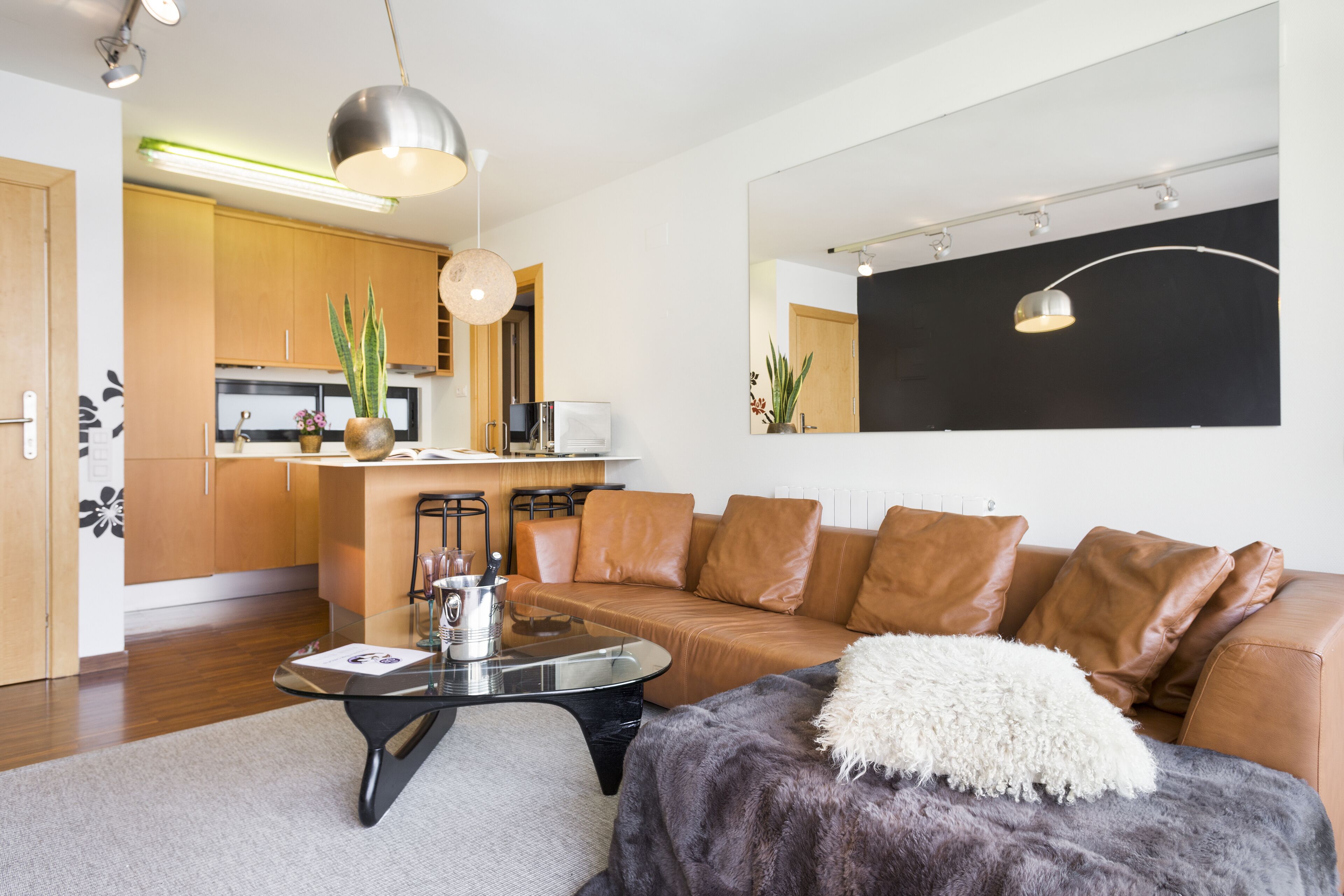 A modern living room with a leather sofa, a glass coffee table, and a large mirror.