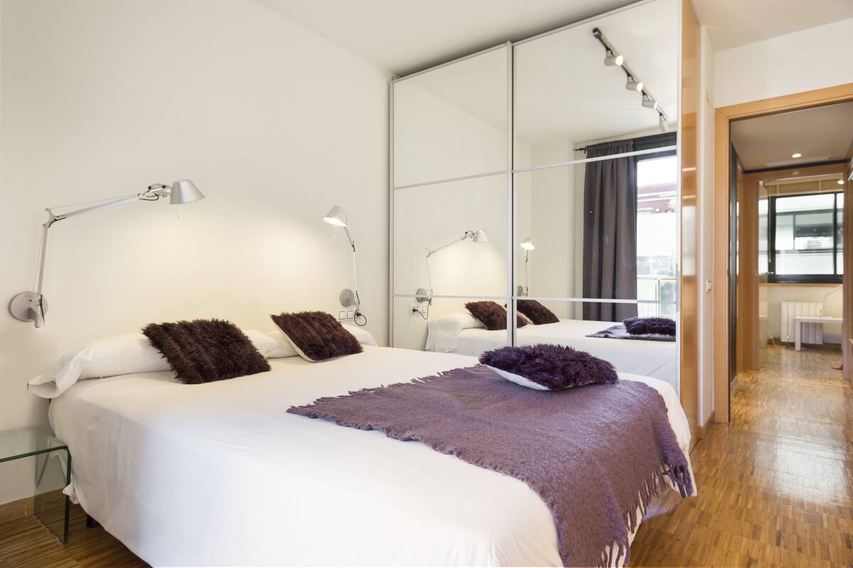 Habitación de hotel moderna con una cama grande, dos lámparas de noche, un espejo y vistas a la ciudad.