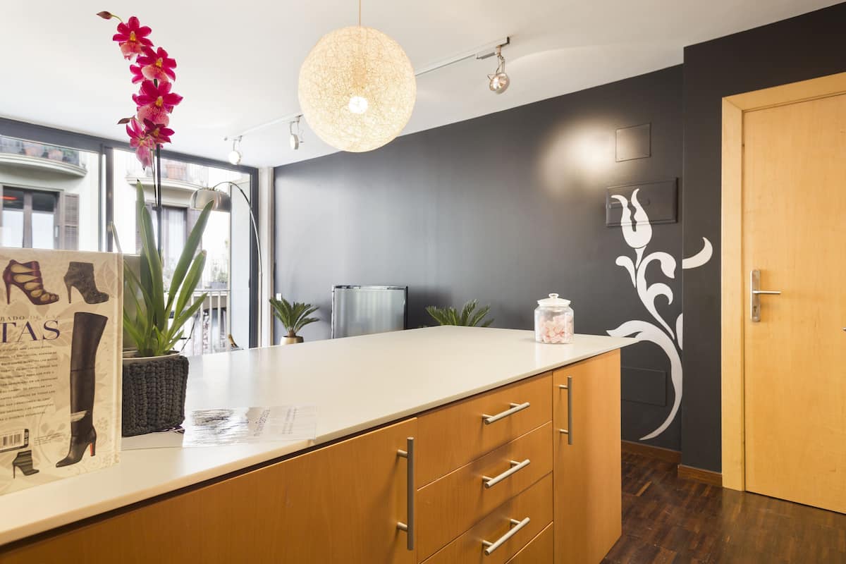Una cocina moderna con encimera blanca, armarios de madera, una lámpara colgante y una orquídea ornamental.