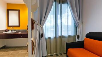 A hotel room with a bed, a bathroom with a sink, and a window with curtains.