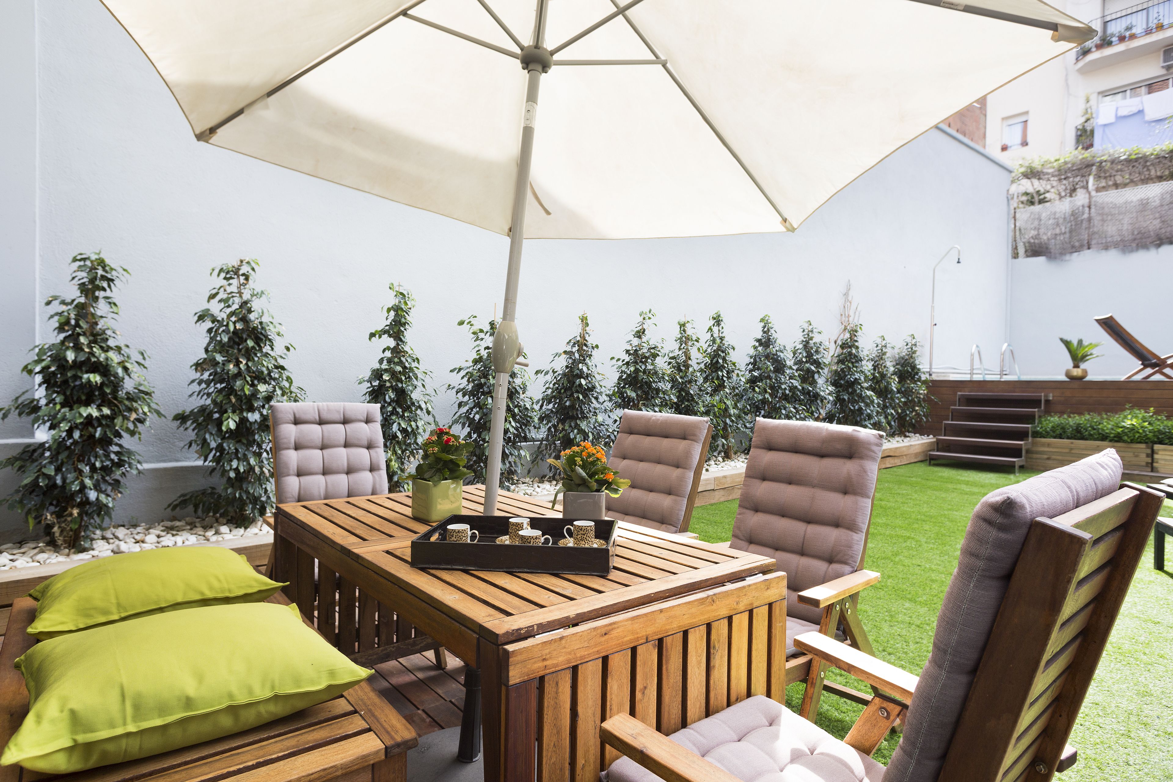 Une table de patio en bois, quatre chaises, un grand parasol et un plateau avec des tasses et une fleur.