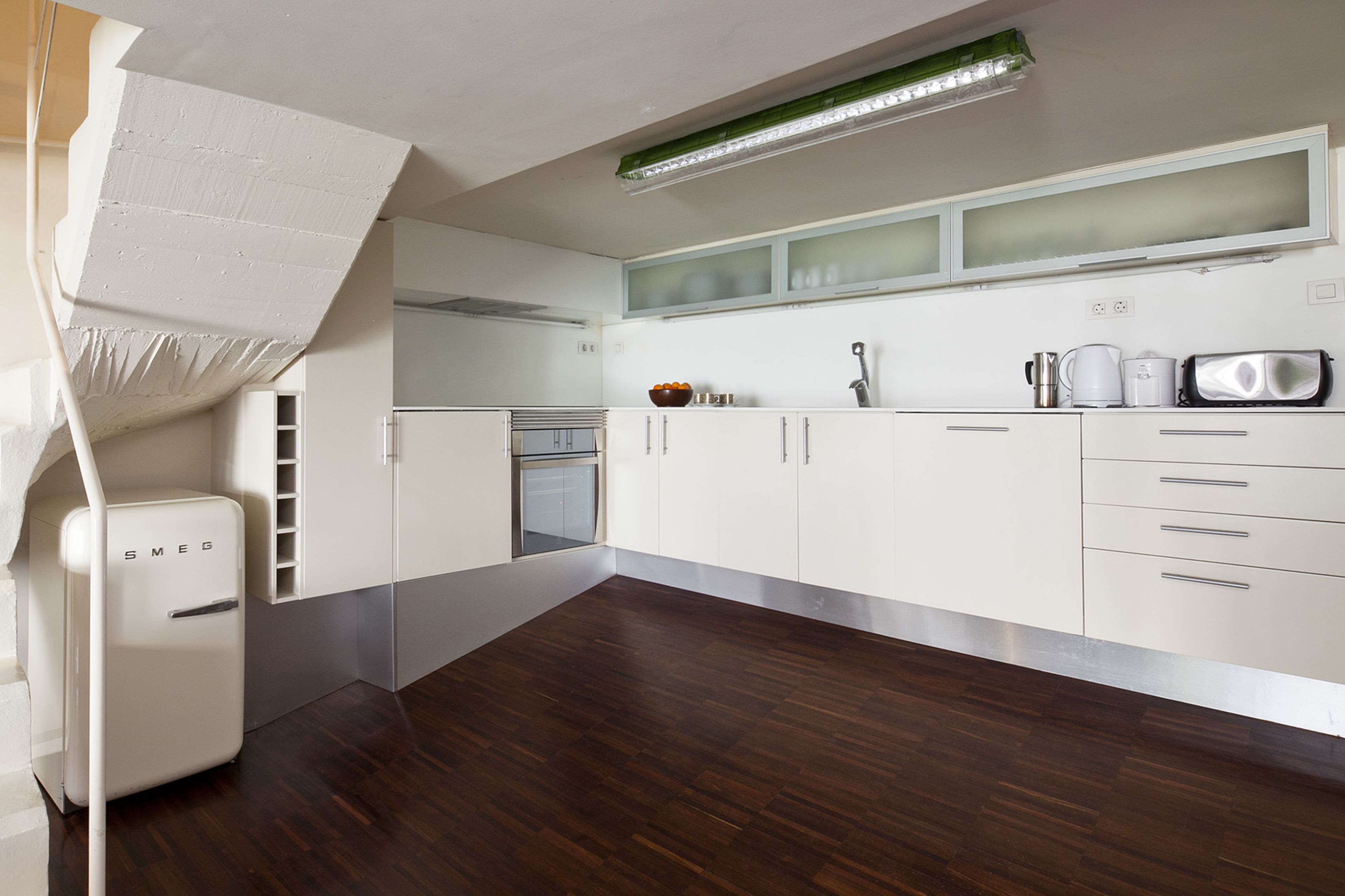 A modern kitchen with white cabinets, a built-in oven, and a stainless steel refrigerator.