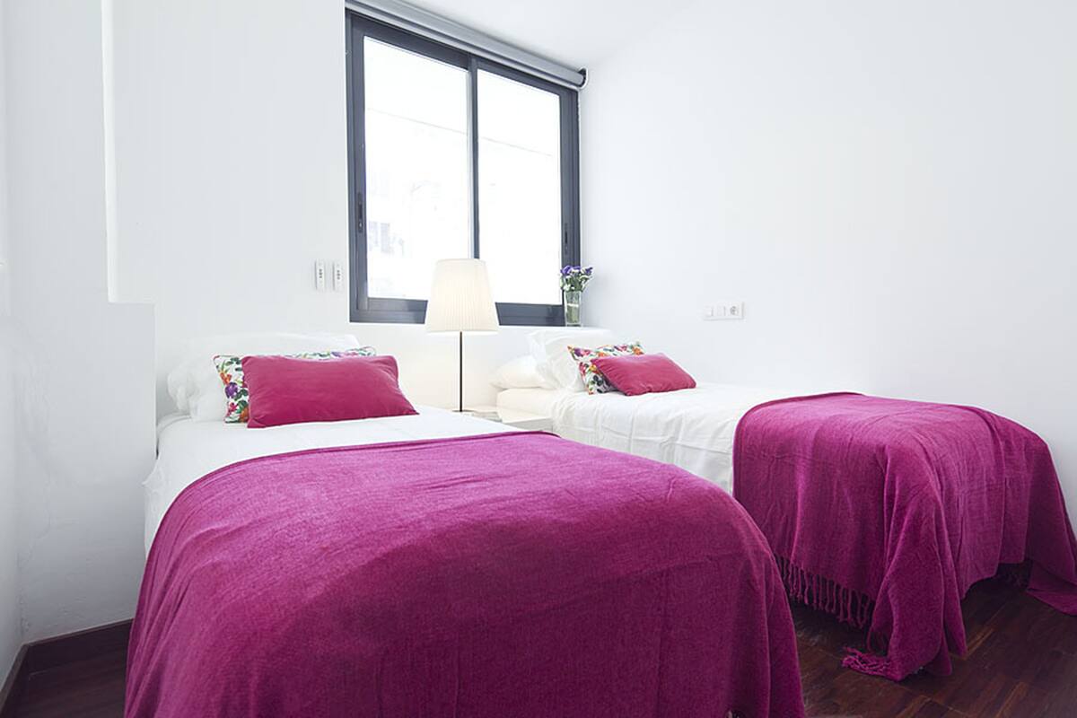 A bedroom with two beds, white bedding, and purple bedspreads.