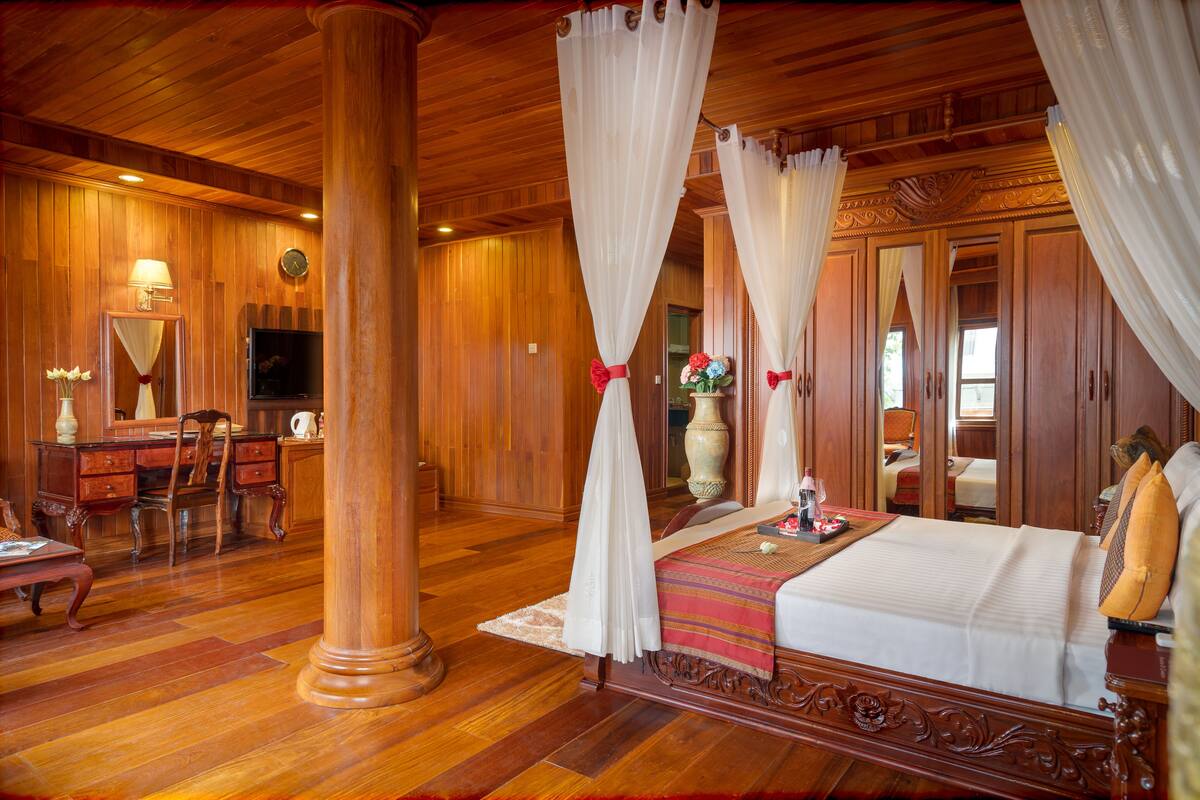 A spacious room with a large bed, wooden flooring, a desk with a chair, and a large mirror.