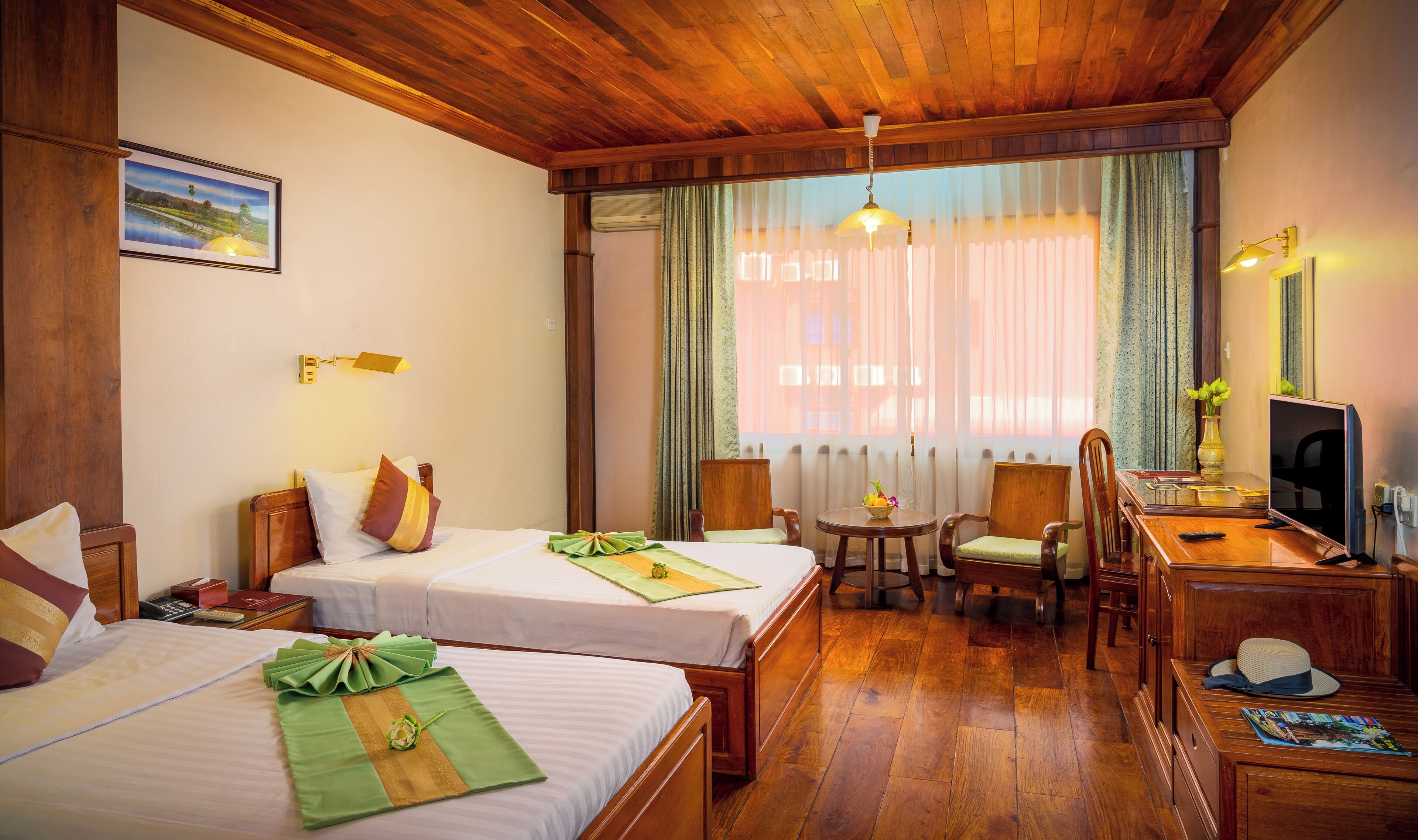 A hotel room with two beds, a desk, a chair, a television, and a window with curtains.
