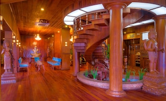 A spacious lobby with a wooden floor, a spiral staircase, and a statue of a figure.