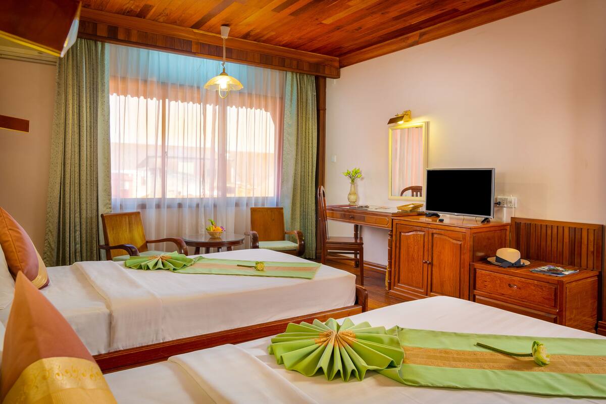 A hotel room with two beds, a desk with a TV, a chair, a wooden cabinet, and a window with curtains.