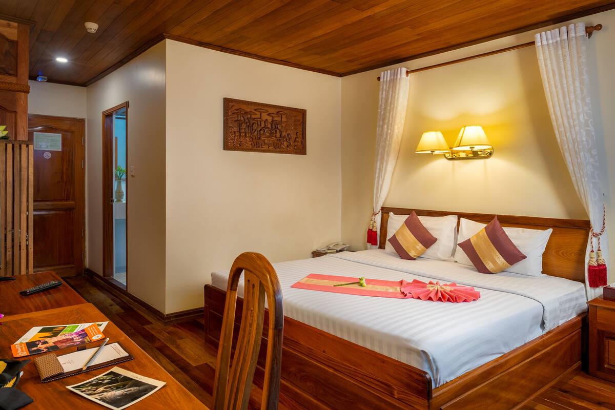 A hotel room with a wooden bed, a desk with a computer, and a door leading to another room.