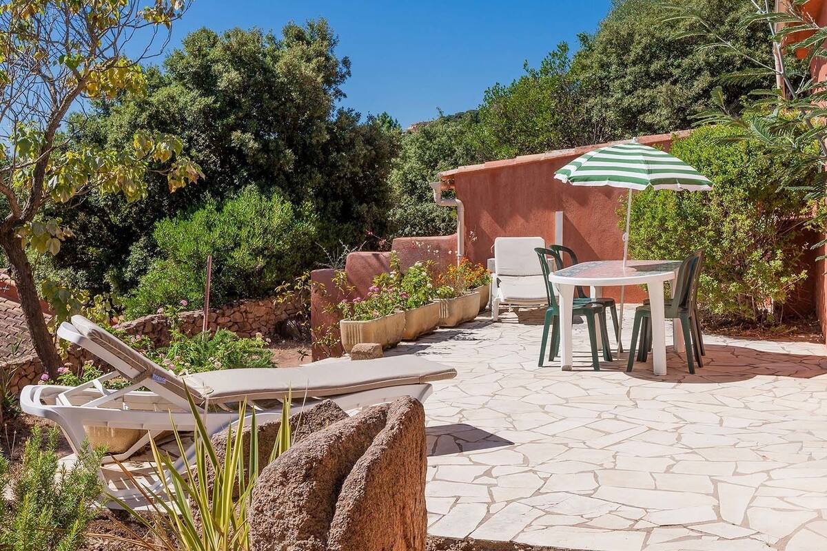 Eine Terrasse mit Tisch und Stühlen, einem gestreiften Sonnenschirm und einem Steinboden.