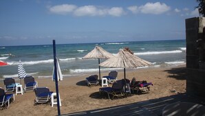 A beach with lounge chairs, umbrellas, and a view of the ocean. - Panorama Hotel Apartments (Hersonissos)