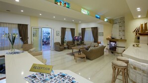 A spacious living area with a reception desk, comfortable seating, a fireplace, and a television. - Panorama Hotel Apartments (Hersonissos)