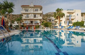Un hotel con piscina, palmeras y montañas al fondo.