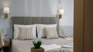 A neatly arranged bedroom with a bed, bedside lamps, a nightstand, and a small potted plant. - Panorama Hotel Apartments (Hersonissos)
