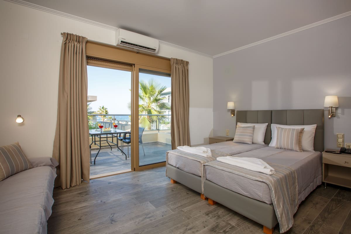 Habitación de hotel con dos camas, un balcón con mesa y sillas, y un equipo de aire acondicionado.