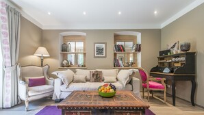 A living room with a sofa, armchairs, a coffee table with fruit, and a piano. - Pension Waldruhe (Grundlsee)