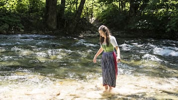 Uma mulher está em um riacho transparente, cercada por árvores.