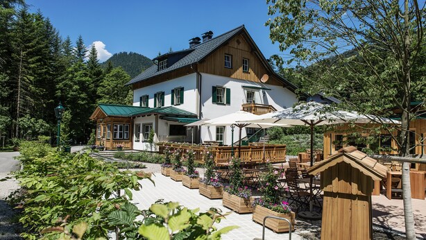 A two-story building with a green roof, wooden balconies, and outdoor seating areas. - Pension Waldruhe (Grundlsee)