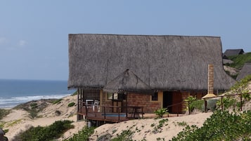 Edifici amb teulada de palla, piscina i mobiliari exterior, amb vistes a una platja i l'oceà.
