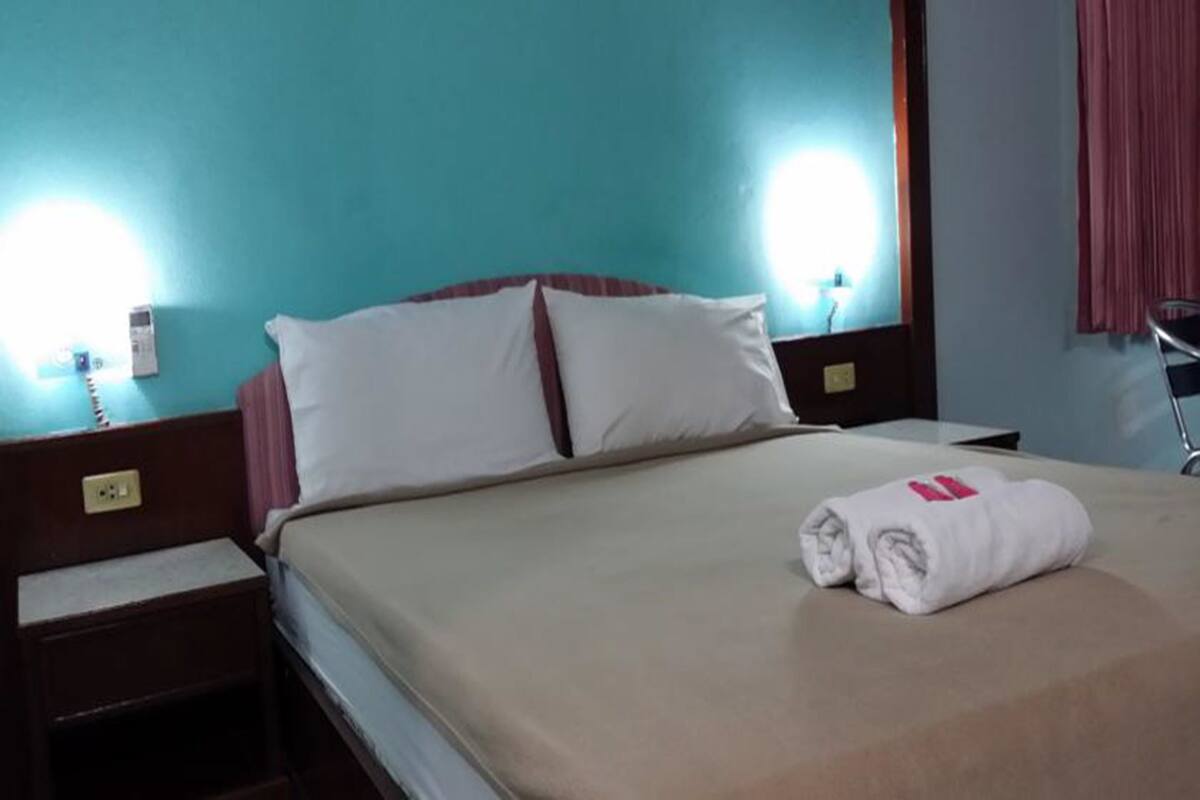 Une chambre d’hôtel avec un lit, une table de chevet et un téléphone fixé au mur.