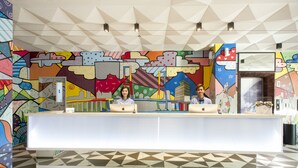 Een receptiebalie met een kleurrijke muurschildering op de achtergrond, een vloer met geometrische patronen en een modern plafondontwerp.
