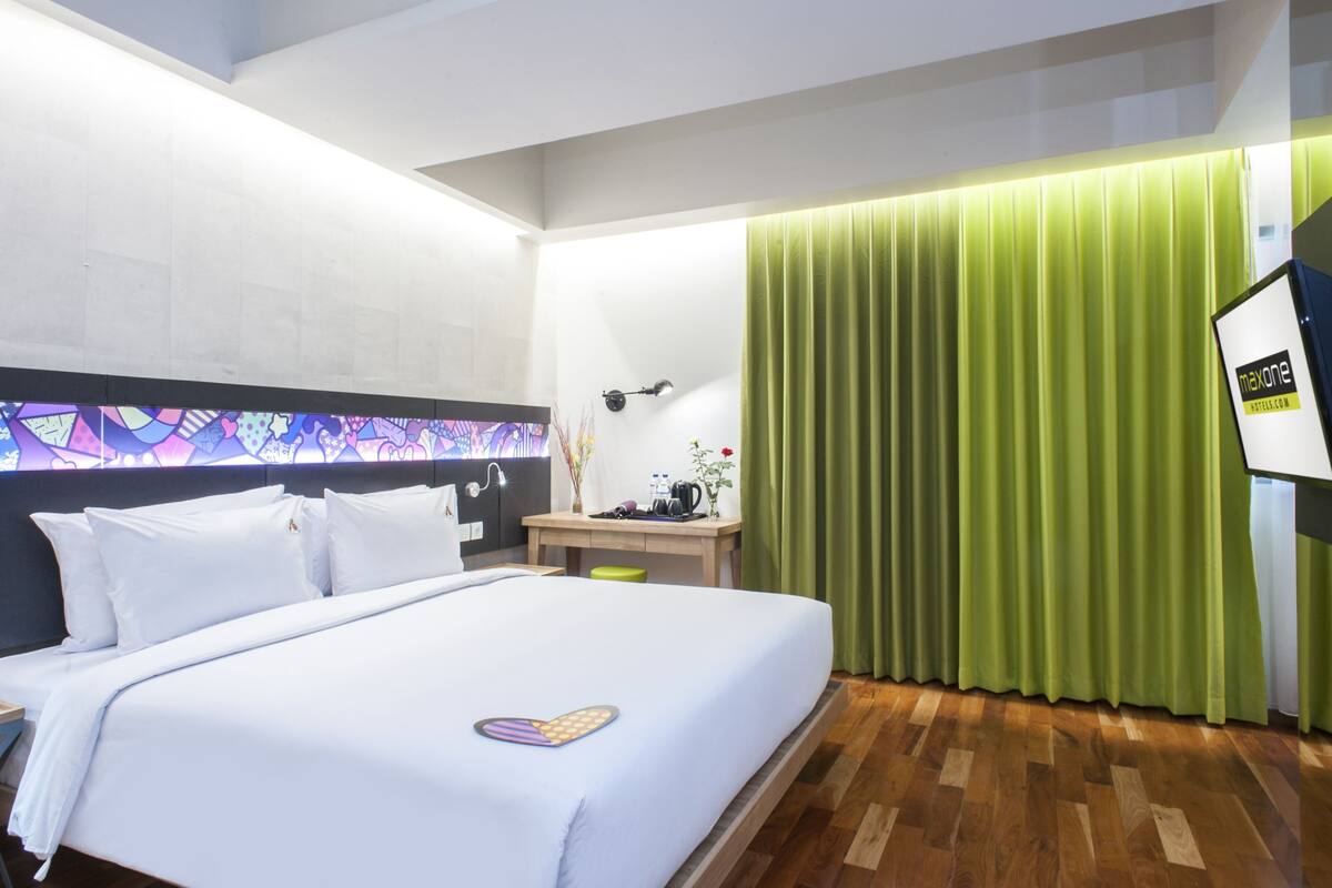 Ein Hotelzimmer mit einem Bett, einem Schreibtisch, einer Lampe, einem grünen Vorhang und einem Fernseher.