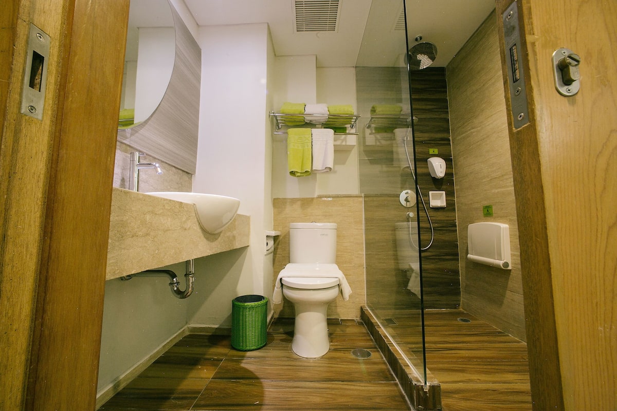 Ein modernes Badezimmer mit Duschkabine aus Glas, Toilette, Waschbecken mit Handtuchhalter und einem grünen Mülleimer.