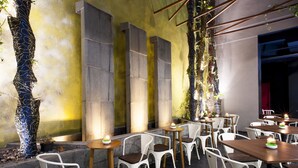 Een terras met witte stoelen en tafels, stenen pilaren en decoratieve planten.